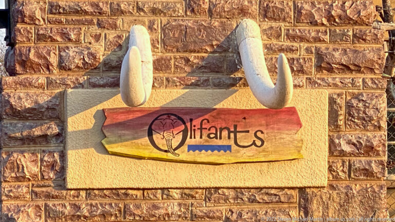 Decorative Olifants sign beneath two white elephant-tusk sculptures on a stone wall.