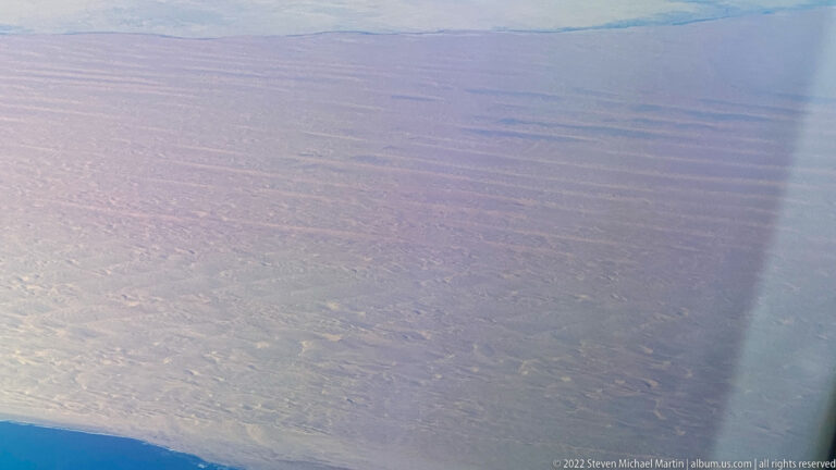 Oblique aerial view of a vast dry landscape with part of an aircraft visible at lower left.