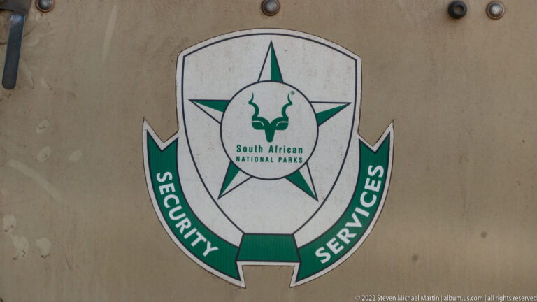Green and white South African National Parks Security Services emblem on a khaki surface.