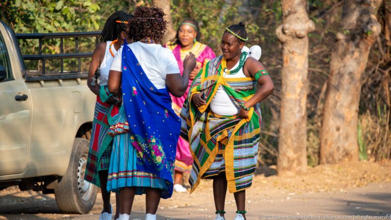 Women wearing colorful patterned garments and beadwork gathered beside a parked safari vehicle.