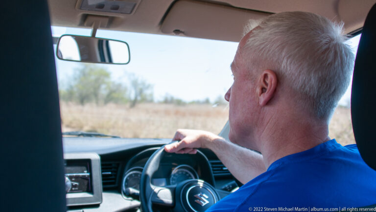 Rear interior view of a person driving a right-hand-drive safari vehicle through dry Kruger grassland.