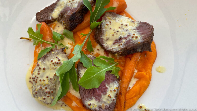 Plate of sliced seared meat with mustard sauce, orange purée, and fresh greens.