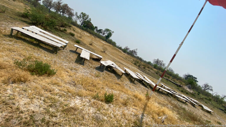 Rows of tilted solar panels on dry ground beside a tall striped pole at a bush airstrip.