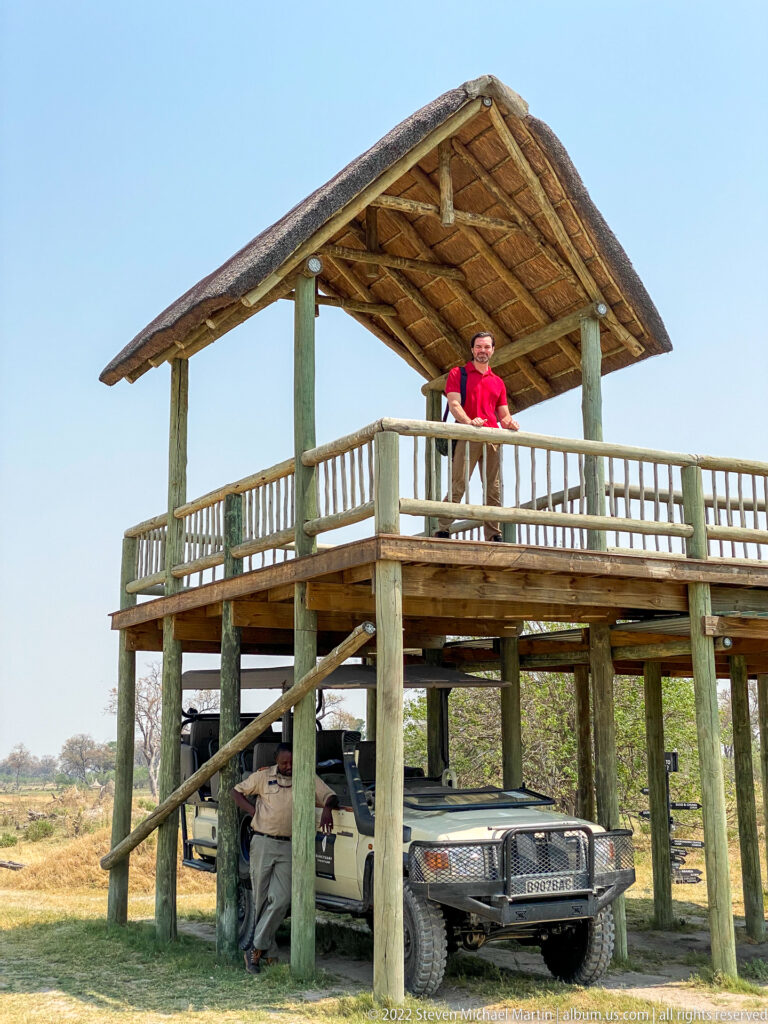 Guest on a raised thatched platform above an open safari vehicle at a bush airstrip.