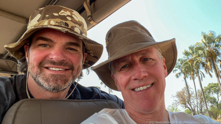 Two smiling adults in sun hats posing closely together inside an open safari vehicle.