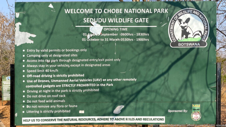 Green Sedudu Wildlife Gate sign reading Welcome to Chobe National Park and listing entry rules, opening times, and conservation regulations.