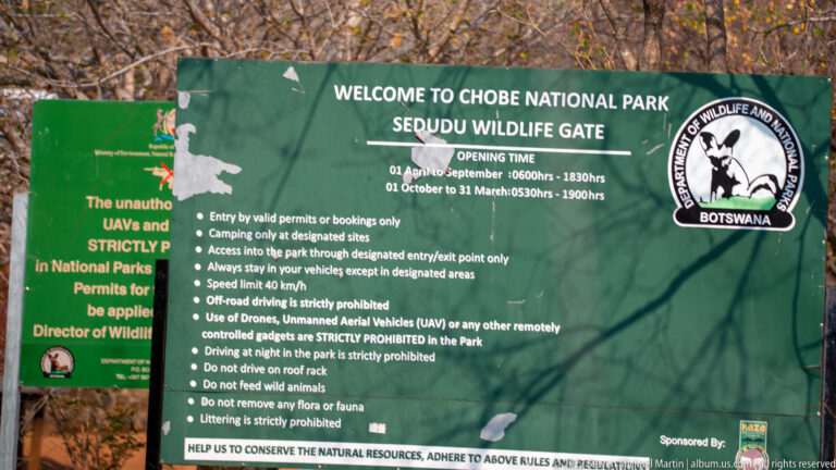 Green welcome and rules sign for Chobe National Park at Sedudu Wildlife Gate among trees.