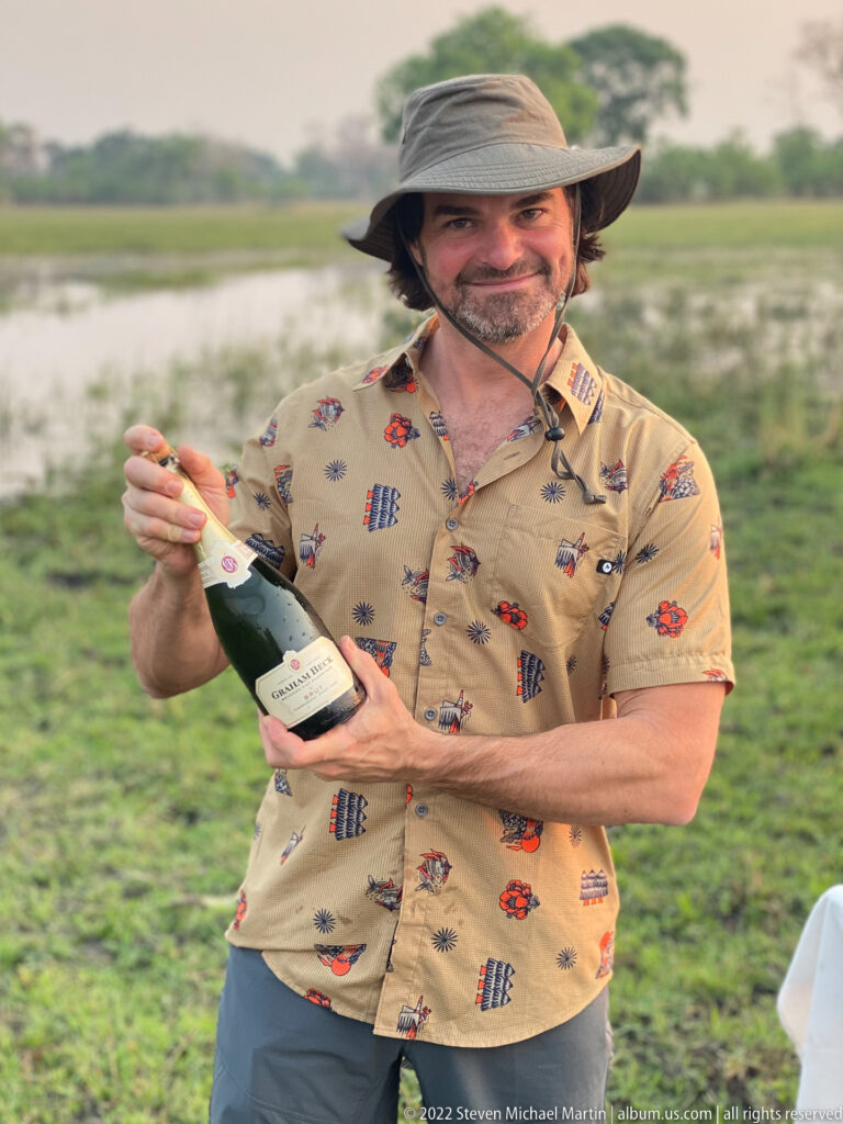 Safari guest holding a bottle of sparkling wine outdoors on the floodplain before opening it.