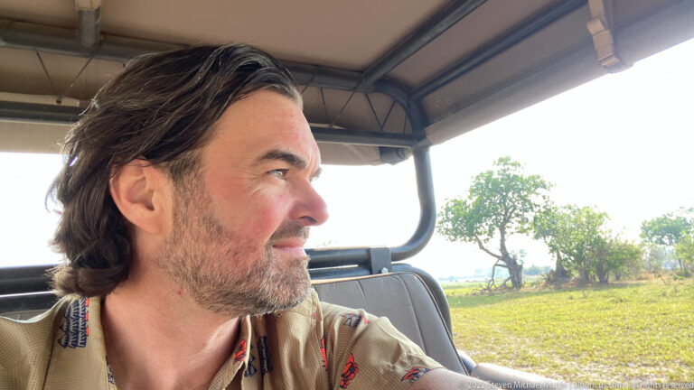 Safari guest seated in profile inside an open game-drive vehicle, looking toward the landscape.