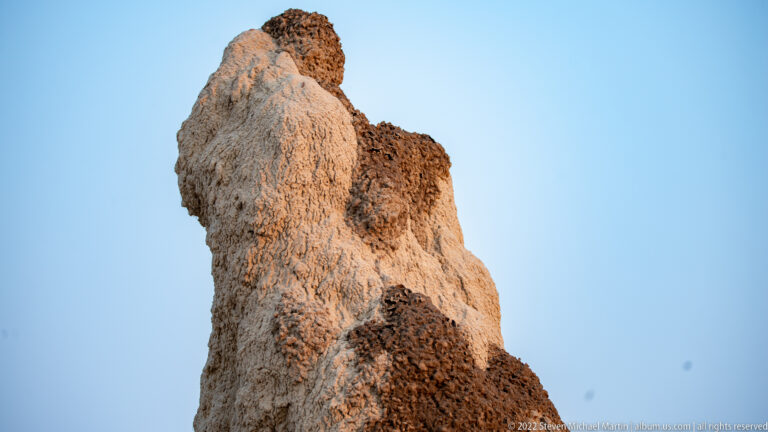 Low-angle view of a tall, lobed termite mound against a clear blue sky.