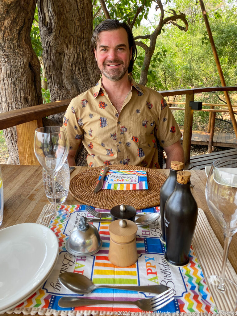 Smiling safari guest seated behind a colorful birthday place setting at an outdoor lodge table.