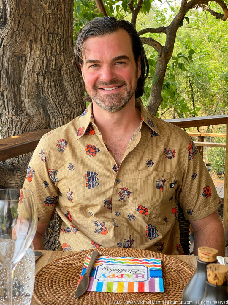 Close portrait of a smiling safari guest seated at a birthday table beneath a large tree.