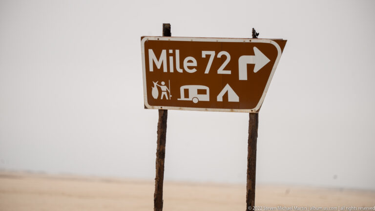 Brown Mile 72 sign pointing right, with angling, caravan, and camping pictograms in the coastal desert.