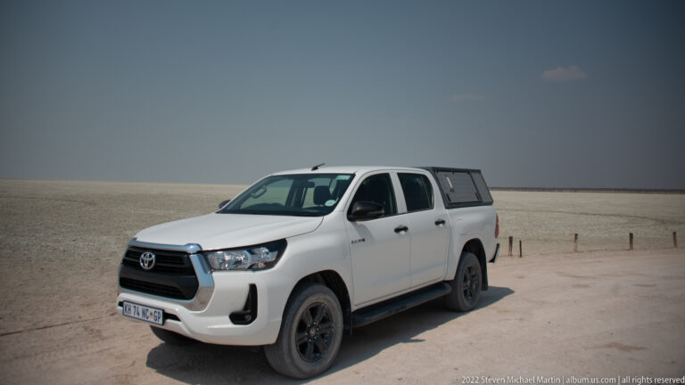 White Toyota double-cab pickup with a rear canopy parked on the pale, flat surface of Etosha Pan.