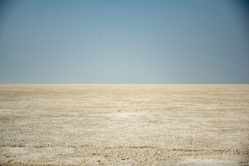 Broad pale salt crust fills the lower half of a minimalist Etosha Pan landscape beneath an uninterrupted blue sky.