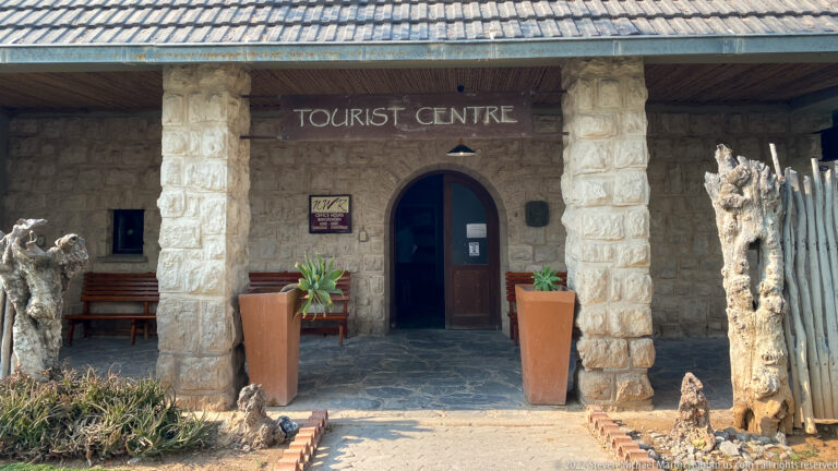 Stone Tourist Centre entrance with an arched doorway, square columns, benches, planters, and the words “TOURIST CENTRE” above.