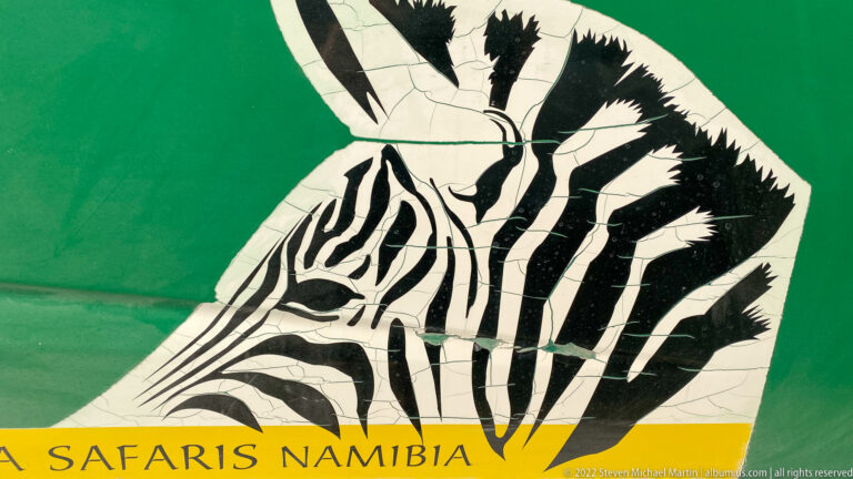 Stylized black-and-white zebra head on green background above a yellow band reading “SAFARIS NAMIBIA.”