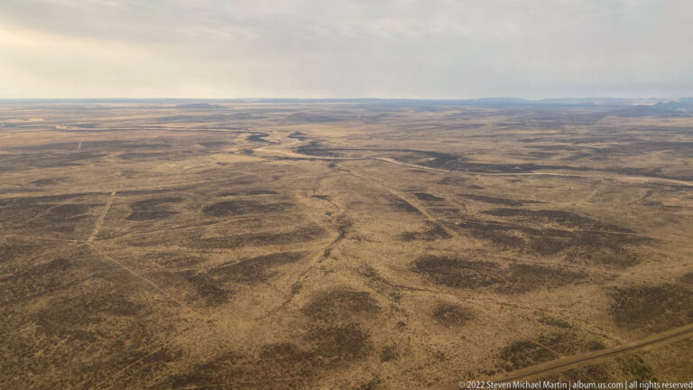 Aerial view of a brown dry plain crossed by pale winding drainage lines and straighter tracks.