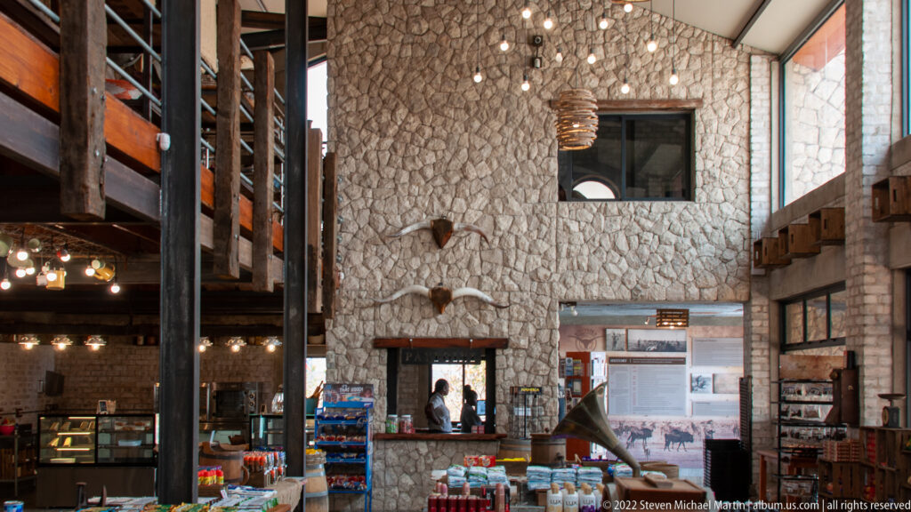 Tall stone wall inside Etosha Trading Post with mounted horned skulls, high window, timber structure and retail counters.
