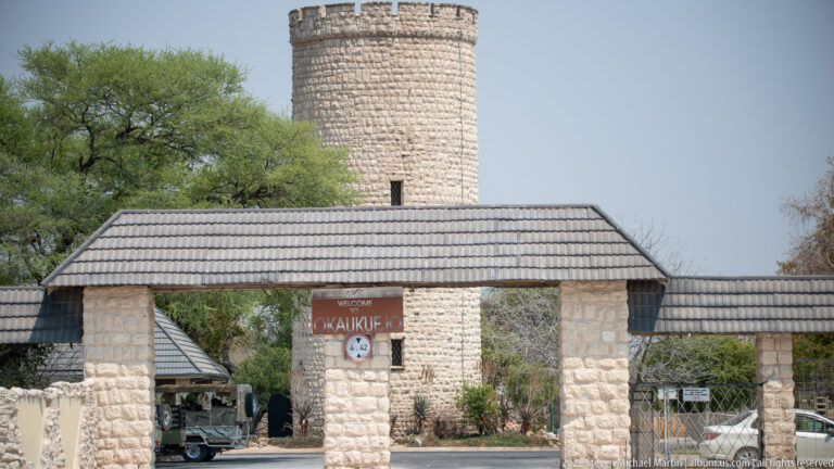 Front view of Okaukuejo entrance canopy and stone pillars with a round crenellated tower rising behind.