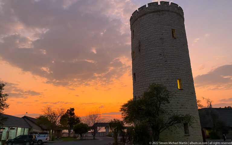Cylindrical crenellated stone tower at Okaukuejo silhouetted against an orange sunrise sky.