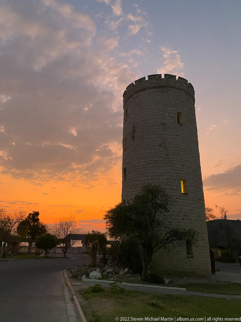 Round stone tower beside a quiet camp road beneath a fading orange dawn sky at Okaukuejo.