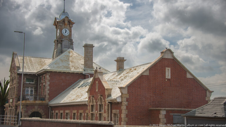 Side elevation of Muizenberg Railway Station with red-brick gables, chimneys, pale trim, and clock tower.