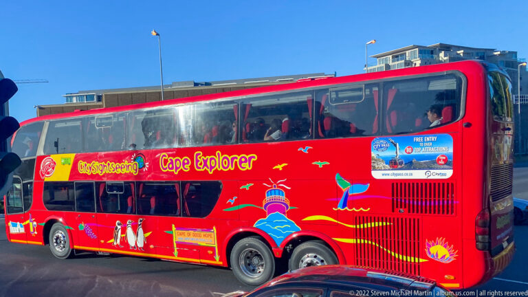 Red Cape Explorer double-decker sightseeing bus with open upper deck and colorful Cape Town graphics.