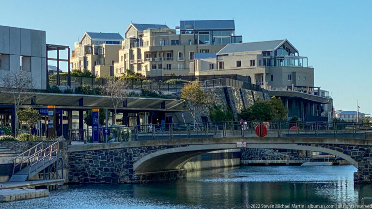 Low stone bridge over a narrow canal, with waterfront terraces and pale multi-story buildings behind.