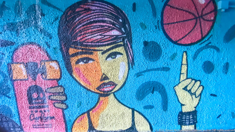 Colorful mural of a stylized young woman holding a pink skateboard, with a basketball above her.