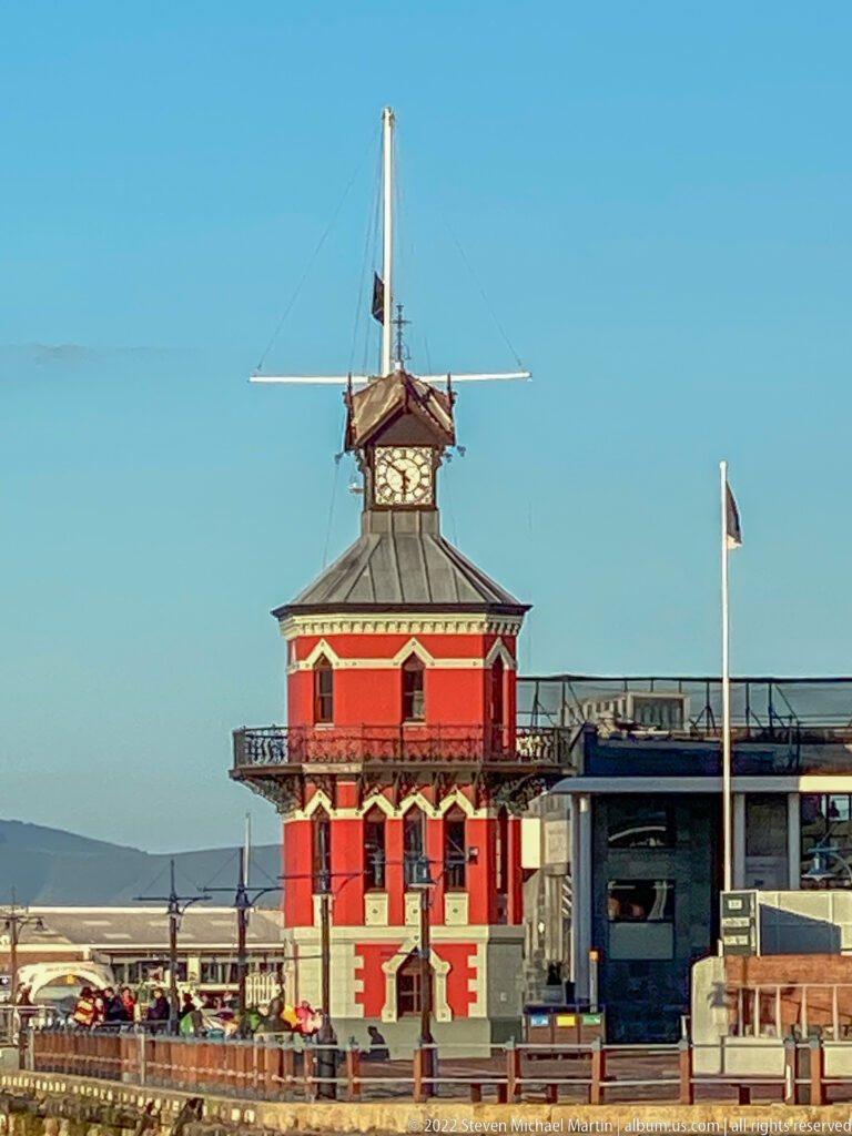 Close view of the red-and-cream V&A Waterfront Clock Tower with balcony, hipped roof, and upper clock stage.