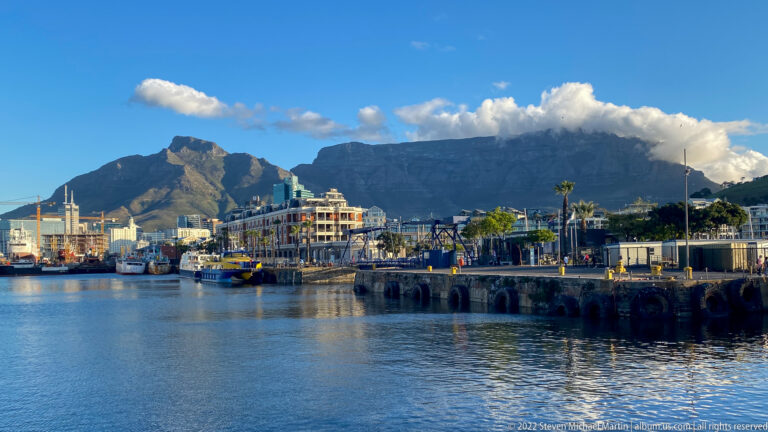 V&A Waterfront harbor with boats and quays beneath cloud-topped Table Mountain.