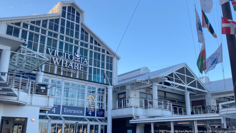 Victoria Wharf Shopping Centre façade with Entrance 4 signs, white steel framing, glass, and flags.
