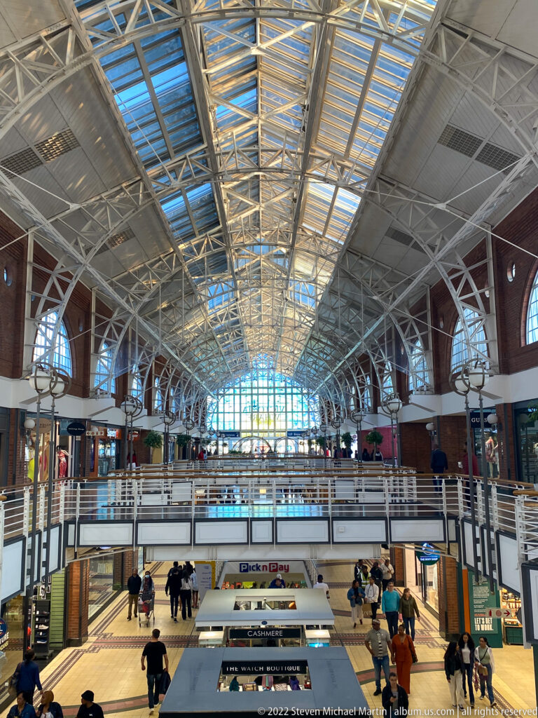 Elevated view across Victoria Wharf’s multi-level shopping hall beneath a broad glazed steel roof.