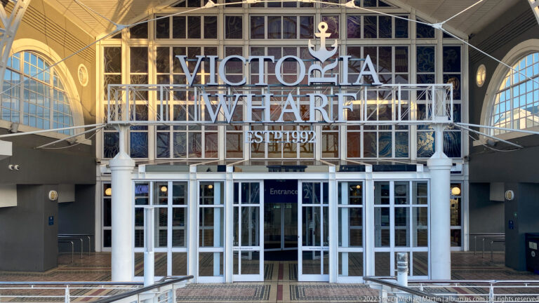 Victoria Wharf entrance with large white lettering, anchor emblem, glass doors, white columns, and steel framing.