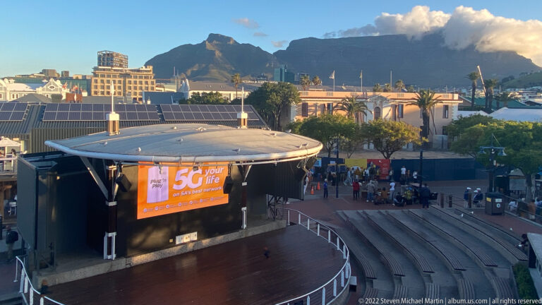Curved outdoor amphitheatre and stage at the waterfront with pedestrians and Table Mountain beyond.