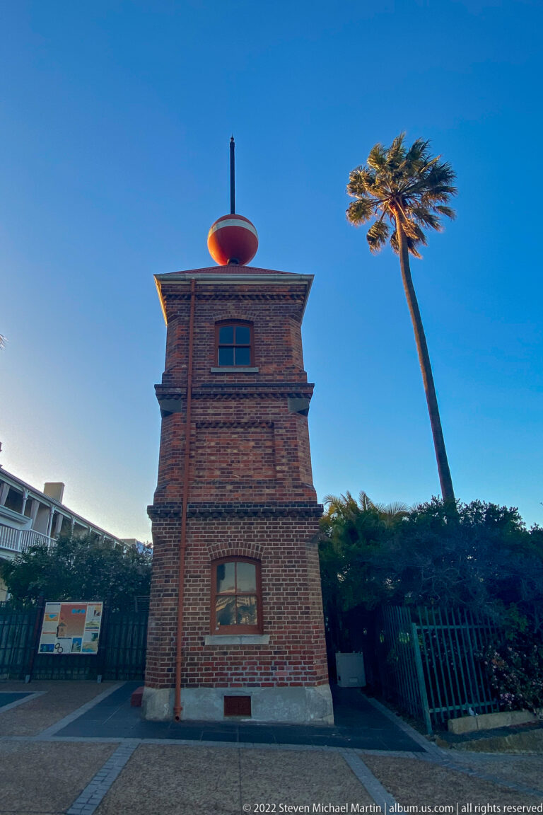 Brick time-ball tower topped by a red sphere, with a leaning palm against blue sky.
