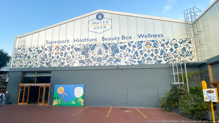 The Watershed building with gabled roof, black-and-white patterned frieze, entrance, and activity signage.
