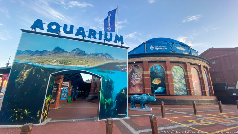 Two Oceans Aquarium entrance with large AQUARIUM lettering, underwater graphics, and a round brick building behind.