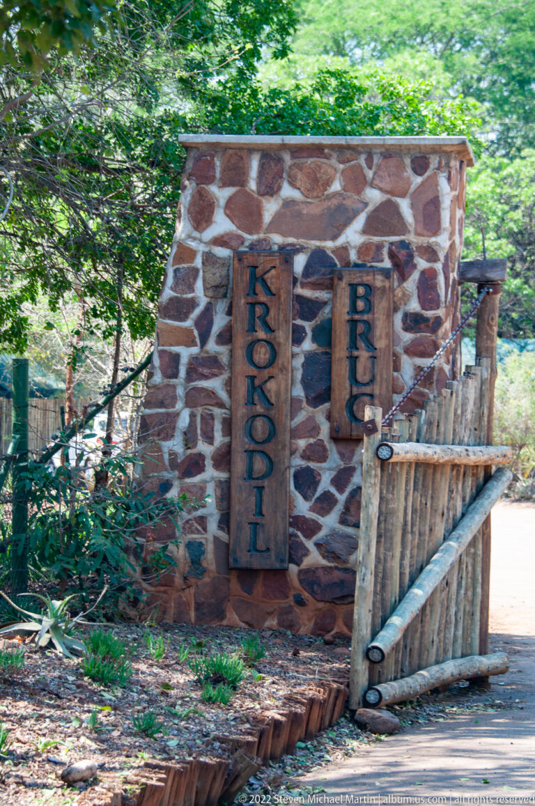 Stone wall with vertical wooden panels spelling Crocodile Bridge beside a timber gate and walkway.