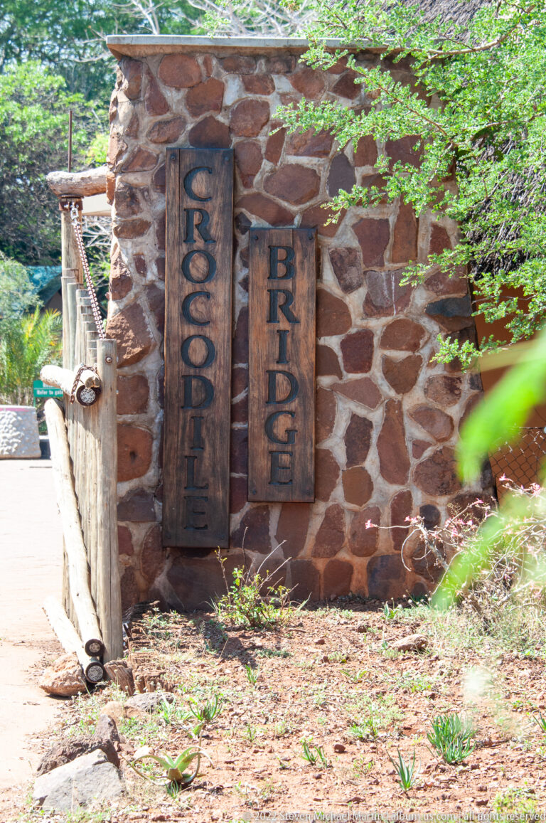 Close view of wooden Crocodile Bridge name panels mounted vertically on a rough stone wall.