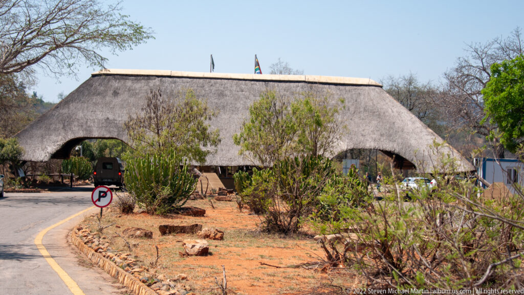 Large thatched-roof gateway building spanning a curved roadway with landscaping and flags above the roof.