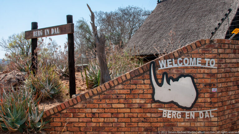 Brick wall reading Welcome to Berg en Dal with a white rhinoceros silhouette and thatched roof behind.