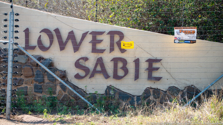 Painted LOWER SABIE lettering on a wall behind a metal gate and security fence.