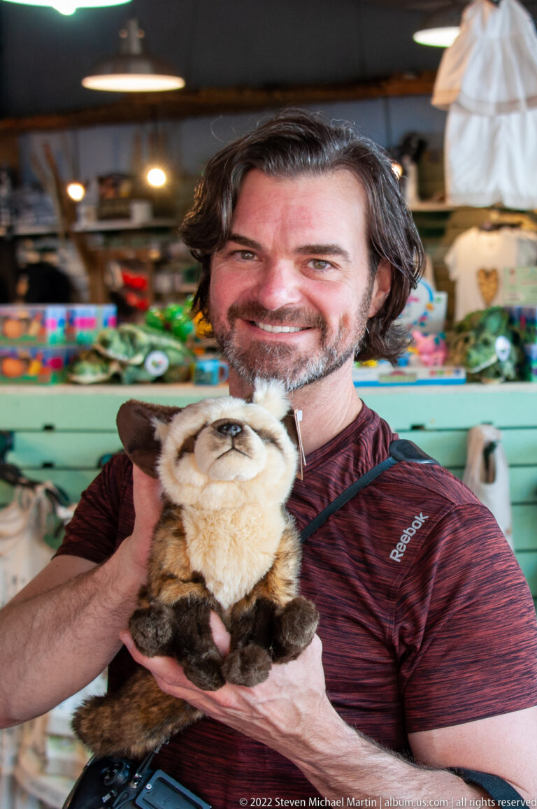Smiling man holding a plush primate toy inside a colorful souvenir shop.