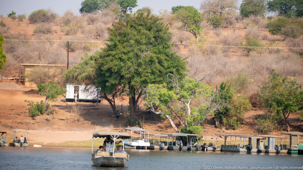 Covered passenger boat on the river approaching a long jetty beside a dry, wooded bank.