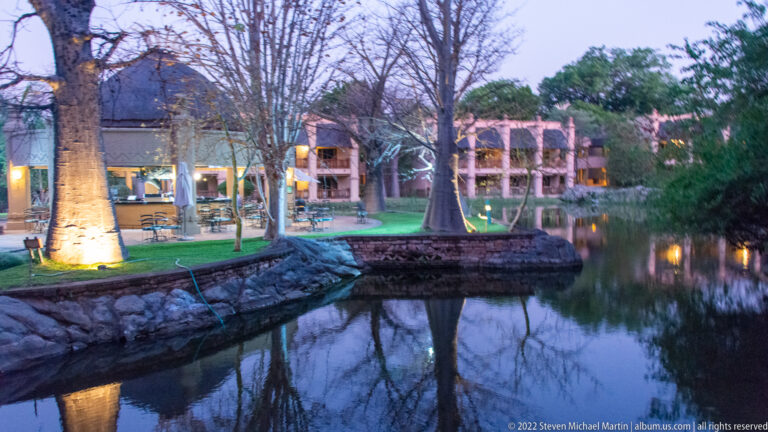 Low resort buildings and trees reflected in a calm landscaped pond at dusk.