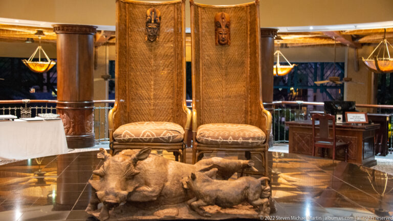 Two tall carved chairs behind a large warthog-and-piglet sculpture on a polished floor.