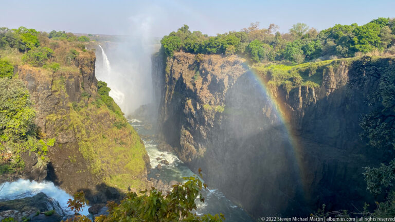 Victoria Falls dropping into a steep basalt gorge with dense mist and a bright rainbow.