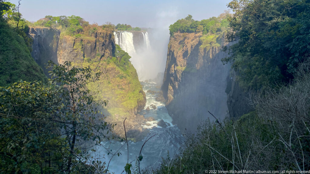 Central waterfall plunging between steep basalt cliffs into the narrow gorge, partly veiled by mist and foliage.